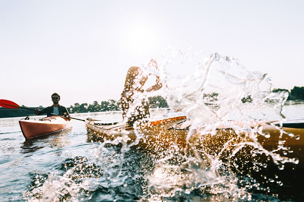 Young couple kayaking on lake together and splashing water