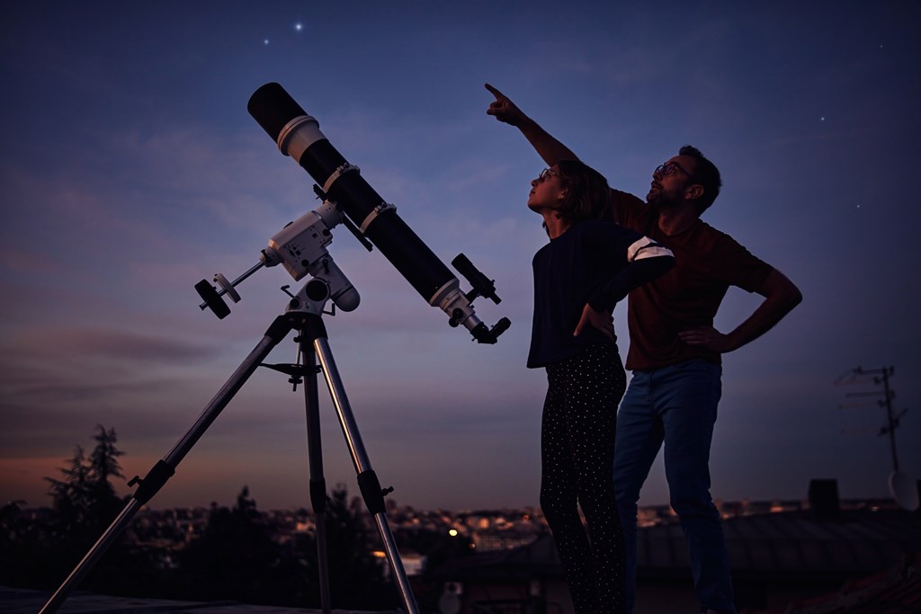 Silhouettes of father, daughter and astronomical telescope under starry skies.