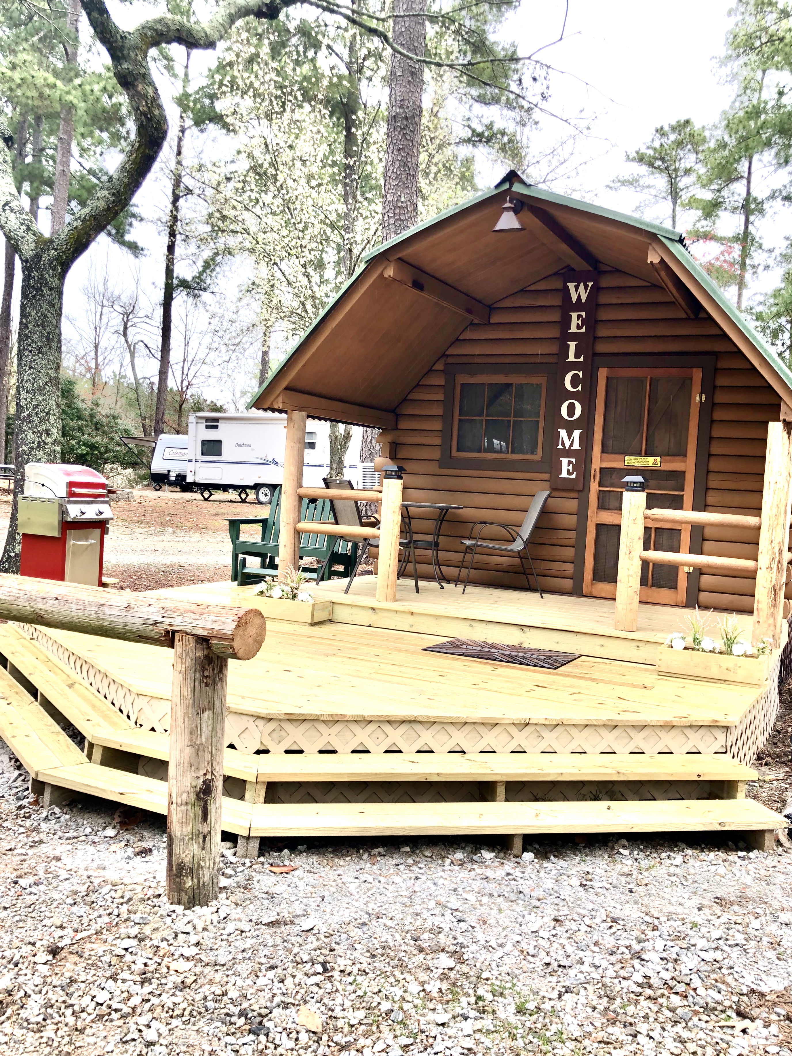 “Cuddle Cabin” exterior. One room camping cabin with a full size bed and a bathroom (sink and toilet only, no shower/tub). Front porch has eating for two, glider, gas grill and fire pit with seating.