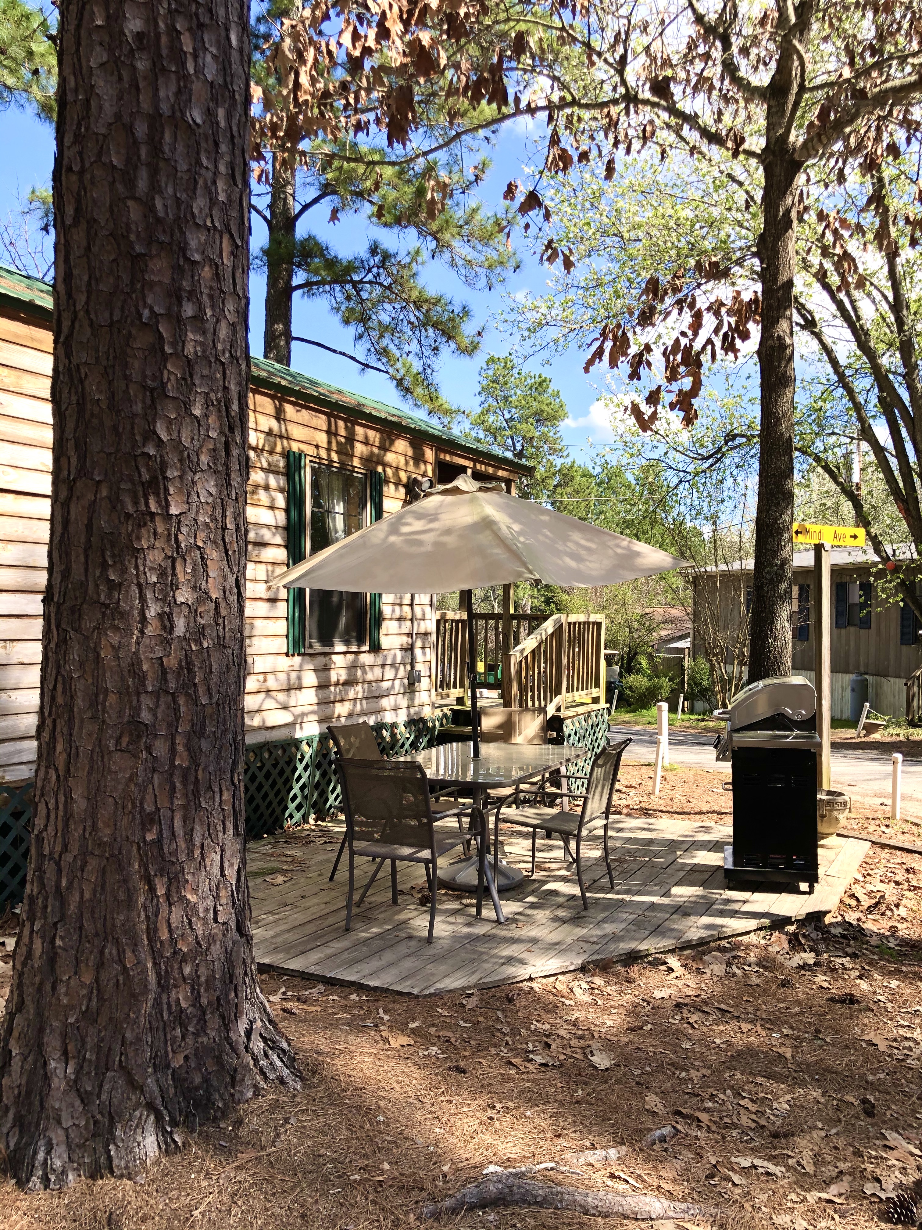 Deluxe Cabin - Park Model. On one side of the cabin is a deck with dining table for five (with umbrella during summer). On the other side, and with more privacy, is the fire pit with a glider and swing.