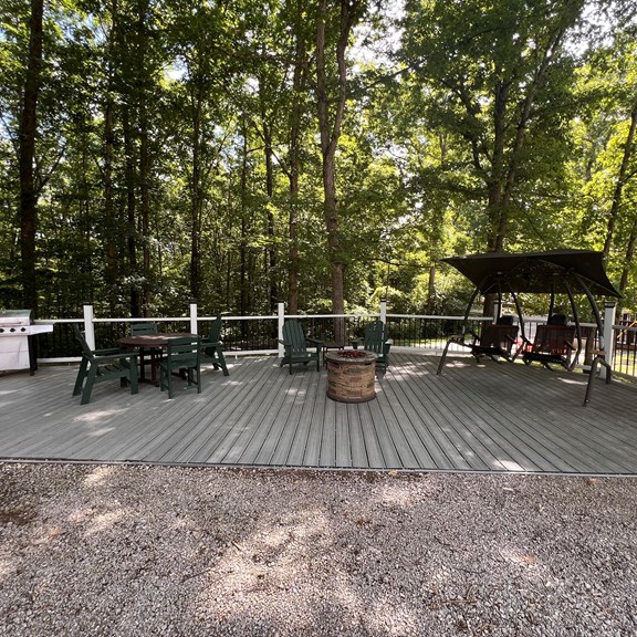 Deck overlooking the trees with Polywood dining set, adirondack chairs, gas firepit  and swing