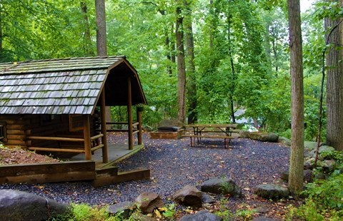 Rustic cabin with porch surrounded by trees at Gettysburg KOA campground