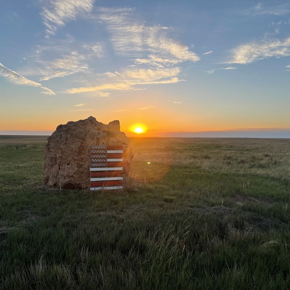Sunset over a historic landmark with a staircase in a grassy field.