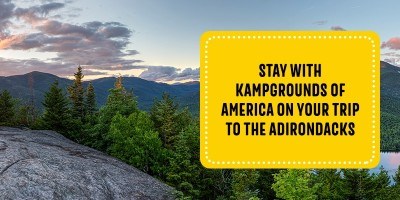 Wide view of Lake Placid, with evergreen trees and mountains at sunset